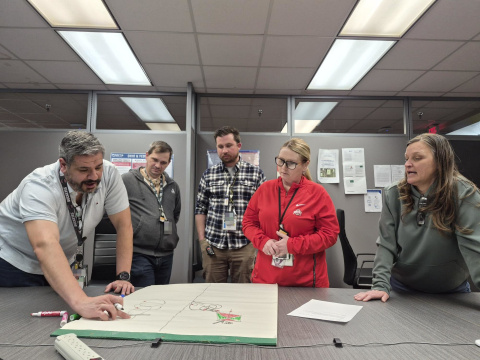 A group of five professionals standing by a table looking at a posterboard on the table