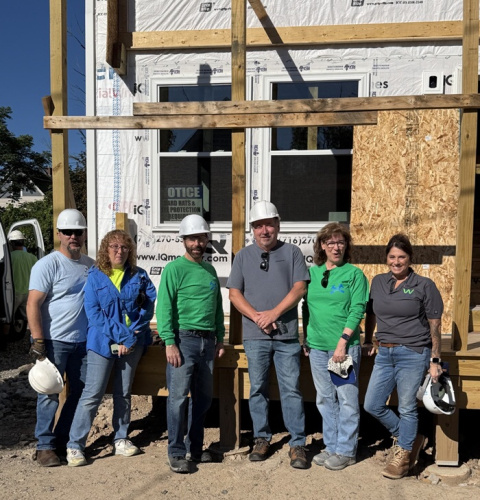 A group of people pose for a photo in white hard hats in front of a house being built