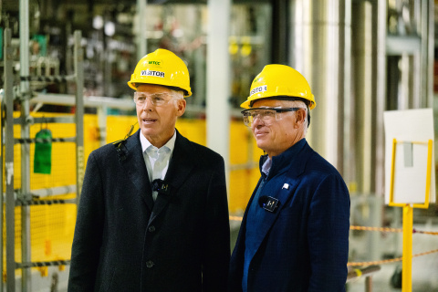 Two professionals standing in a laboratory building wearing yellow hard hats