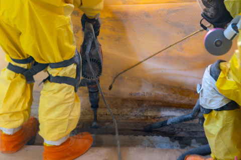 An up close shot of workers in yellow hazmat suits spraying liquid on a wall