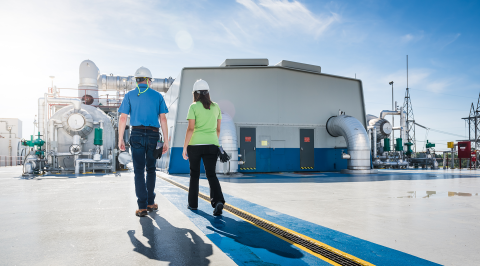 Two workers wearing hard hats walk past the steam turbine building at Robinson Nuclear Plant.