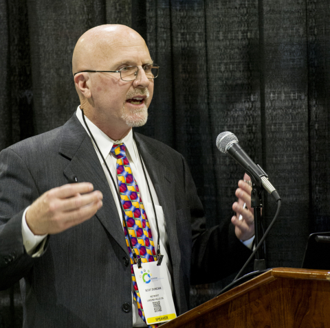 Photo of a man in a business suit speaking at a microphone.