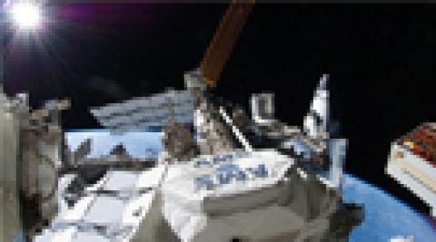 The AMS is visible on the ISS just after being installed, with a US Space Shuttle docked on the far right, a Russian Soyuz capsule docked on the far left.