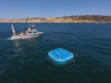 Cal Wave's WEC floating in the open ocean with a small boat behind it 