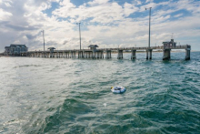Image of the hydraulic and electric reverse osmosis (HERO) floating in the surf with a pier in the background
