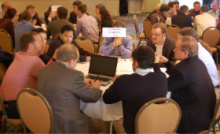 People sitting at round tables in a convention hall.