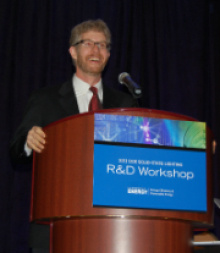 Man in a suit and tie standing at a lectern addressing an audience.