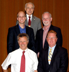 Five men in business attire standing together facing the camera.