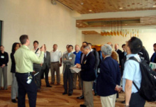 Group of people standing in a convention hall area with one man addressing them.