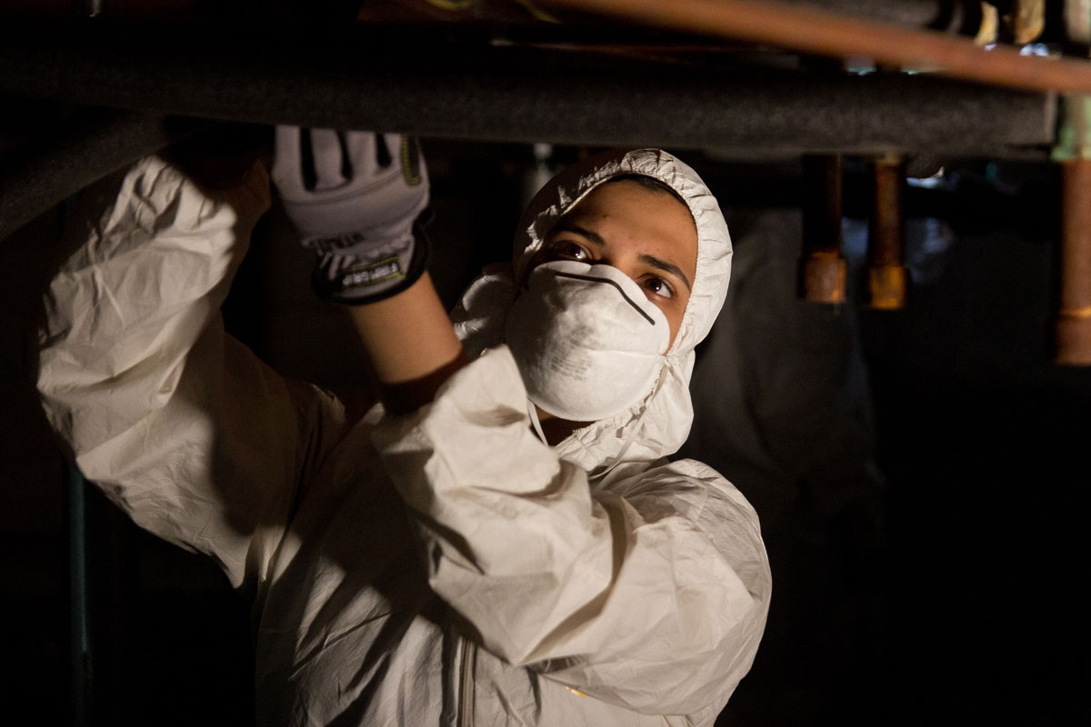 Person in a respirator installing pipe wrap insulation.