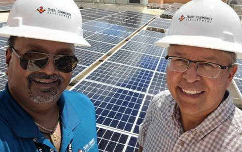 Two men with hard hats pose with roof top solar panels.
