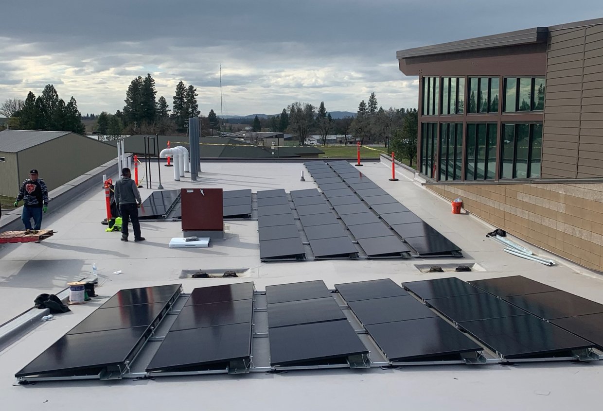 Two men install solar panels on a youth center roof.