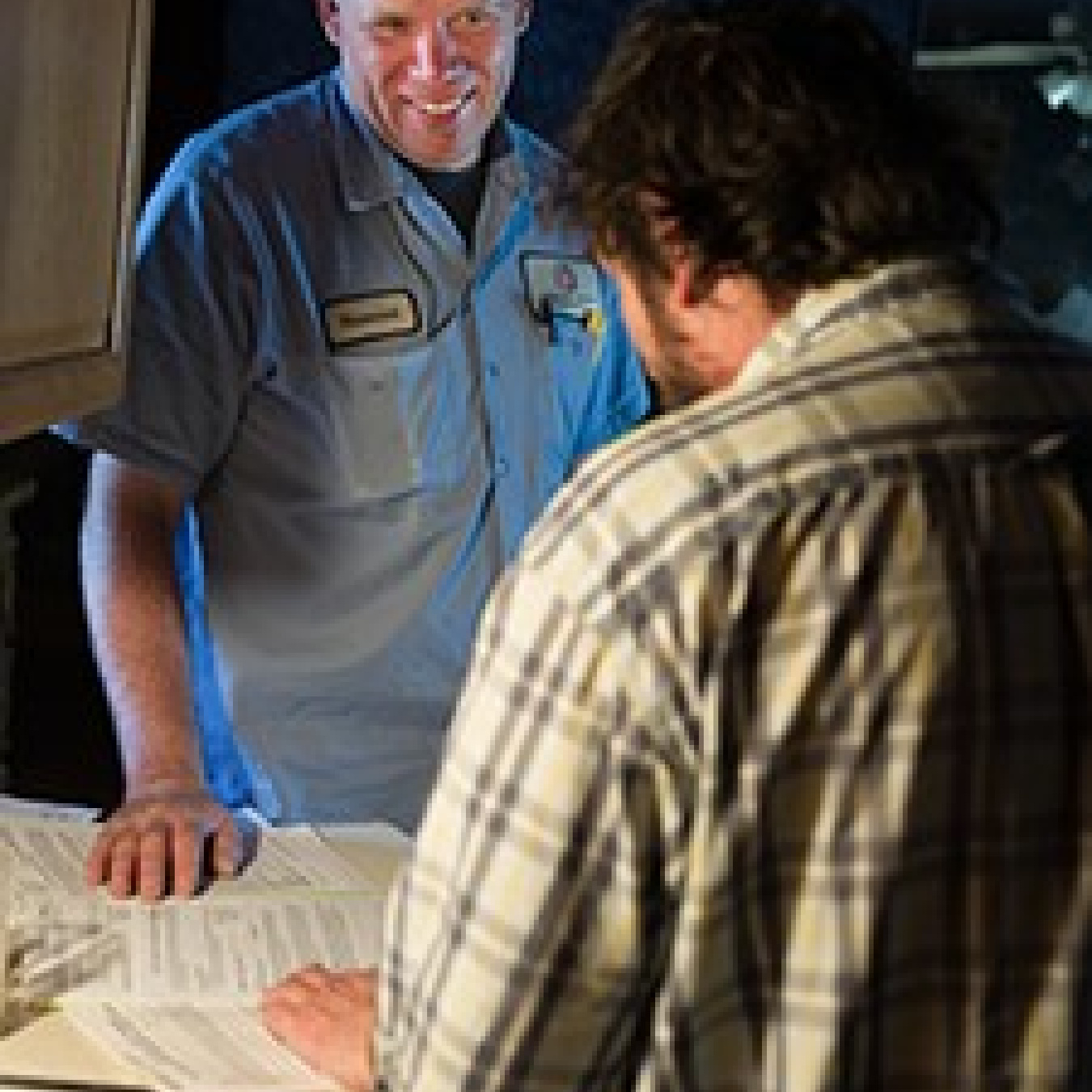 Photo of two men standing and talking. One of the men wears a workshirt with his namepatch on it.