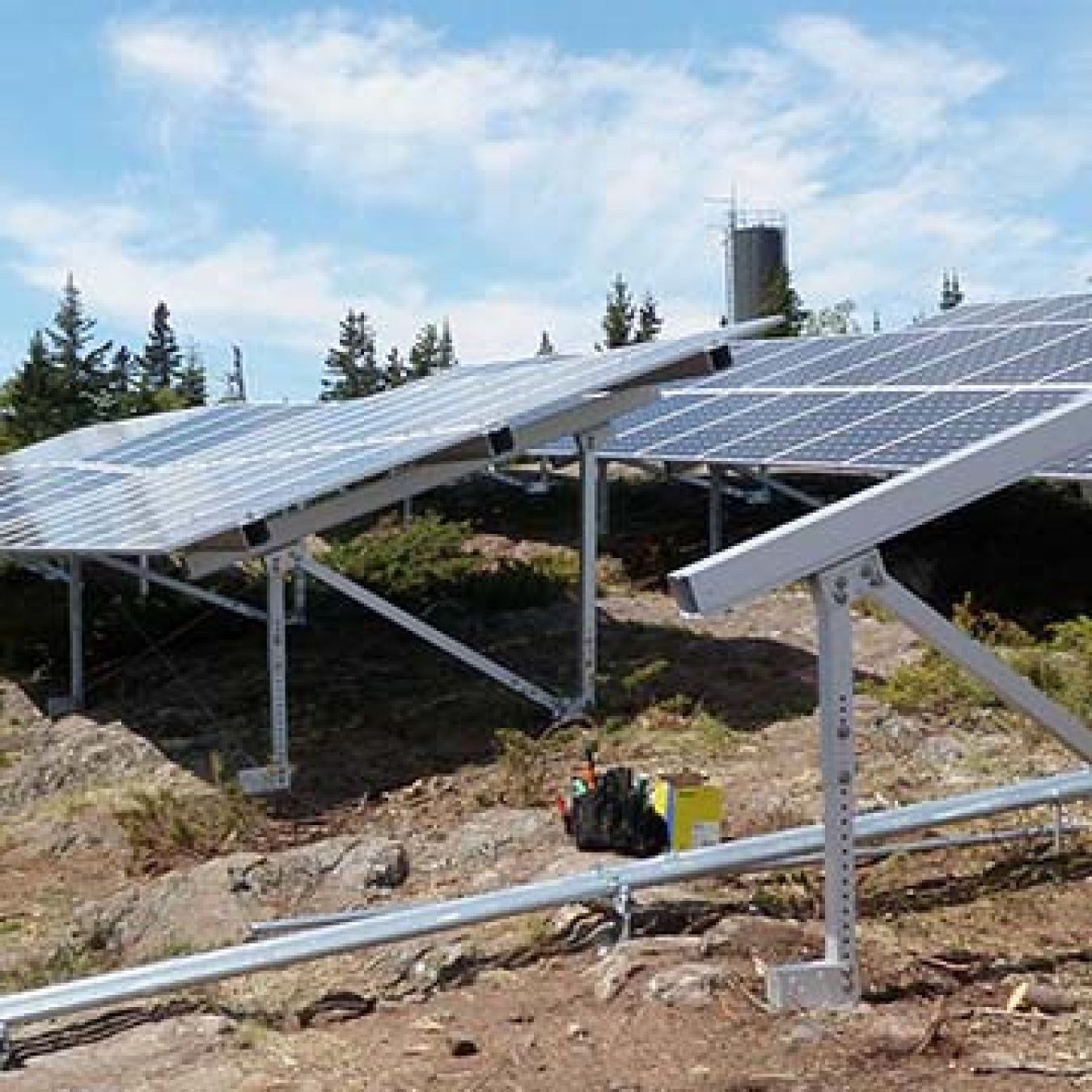 Two rows of solar panels on the side of a rocky hill.