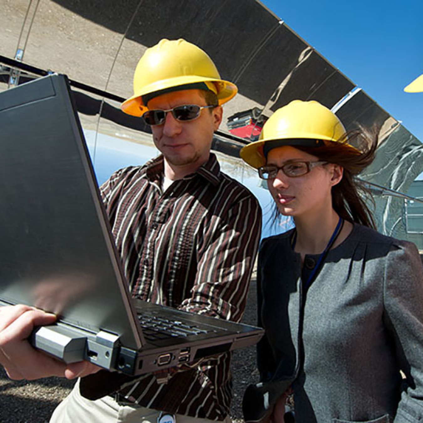 Three people looking at a laptop computer on a worksite.