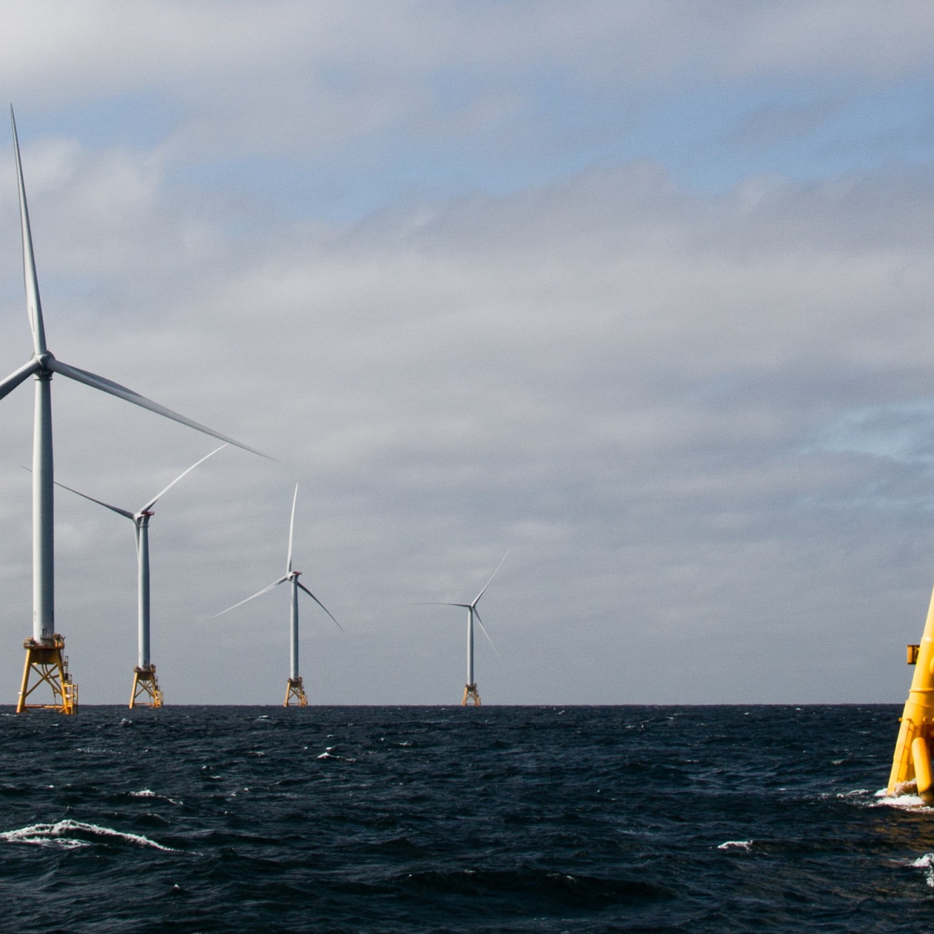 Offshore wind turbines at sea with sun shining.