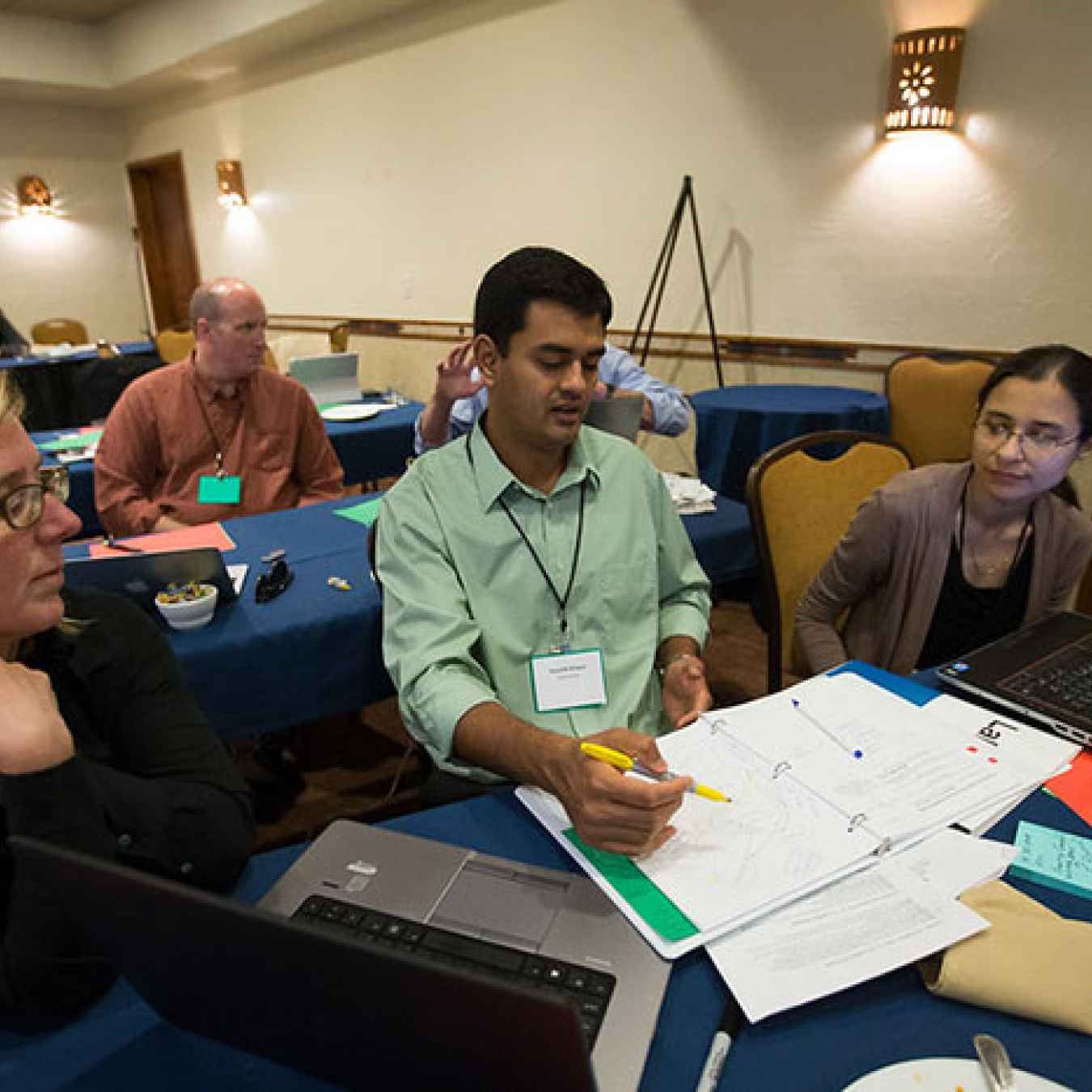 A team of two women and a male work on a project together at a table covered with papers and laptop computers.