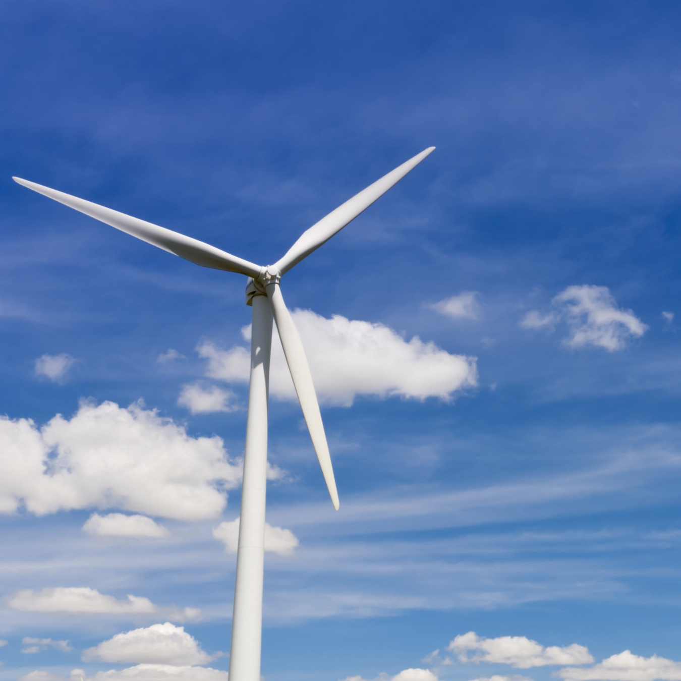 Wind turbine against a sunny sky with clouds.