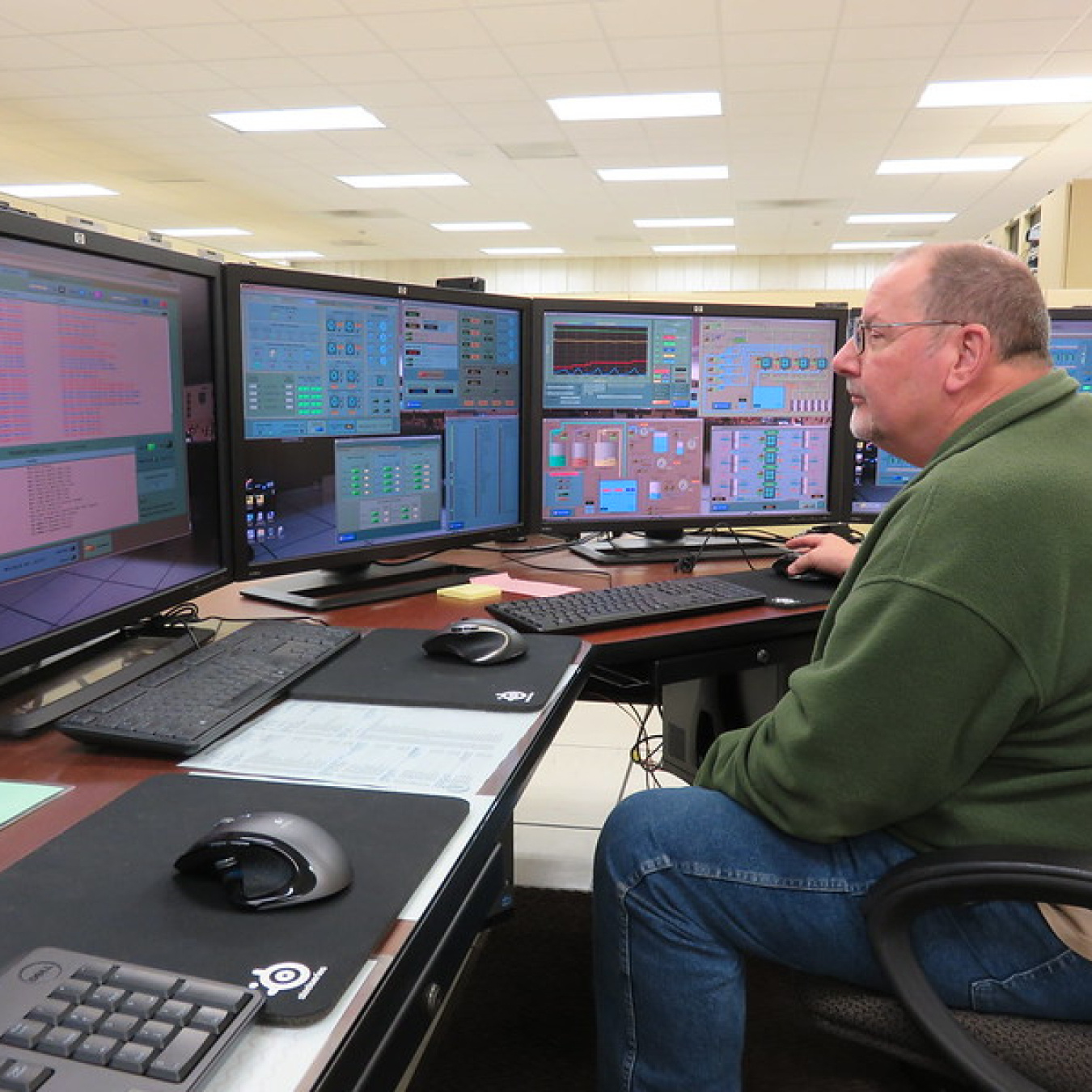 An employee sits looking at computer monitors. 