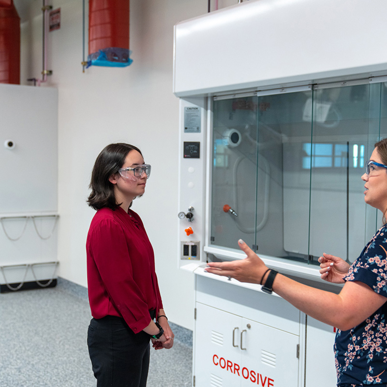 Two female scientists standing in front of lab equipment having a discussion.
