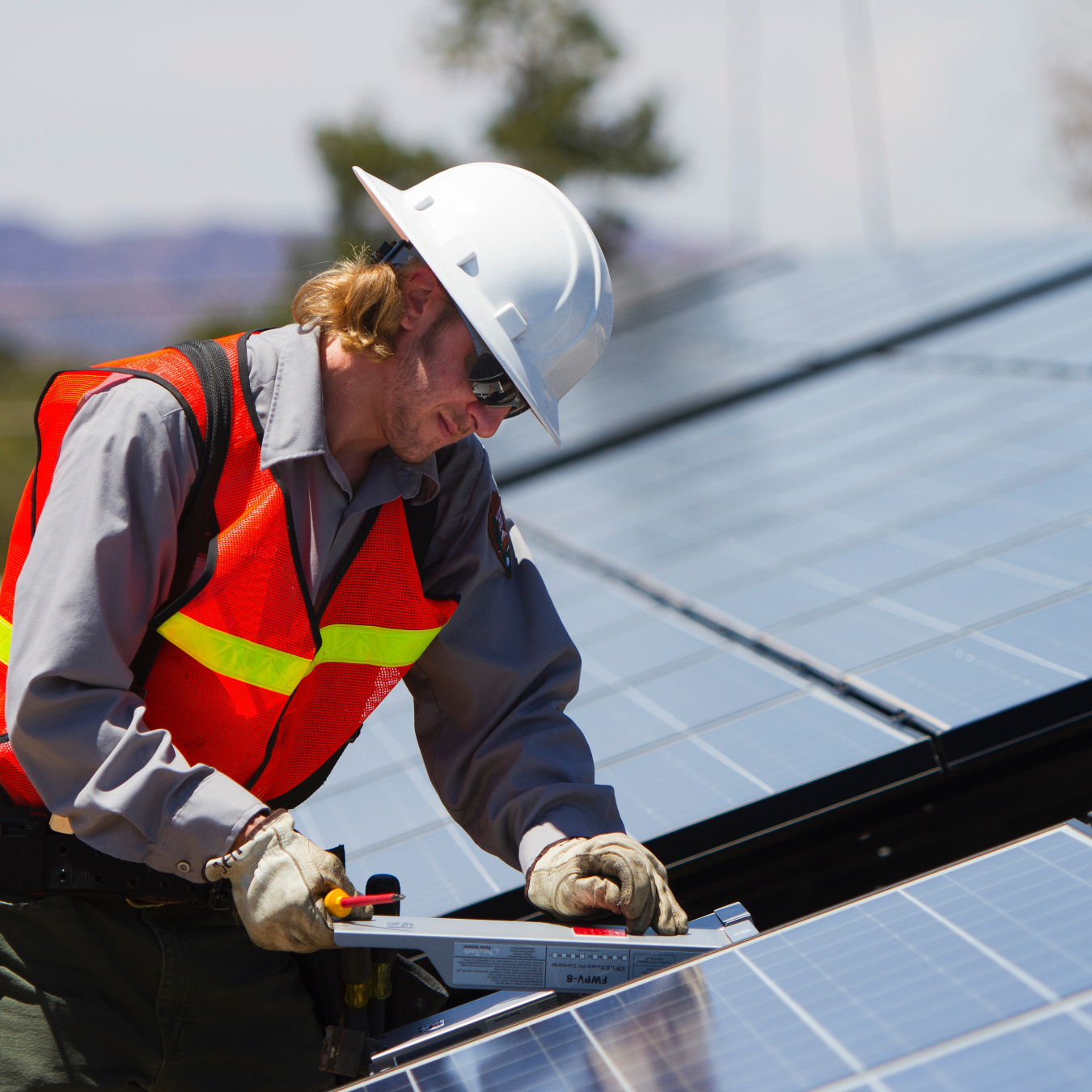 Photo of a man in an orange vest and hard hat performing maintenance on a PV array.