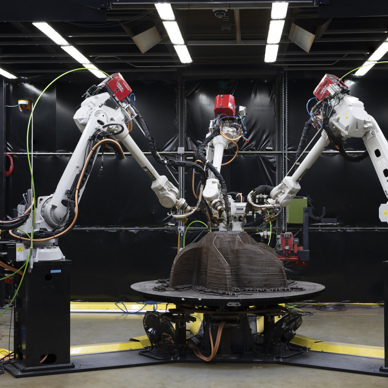 Large mechanical arms construct a metal object. 