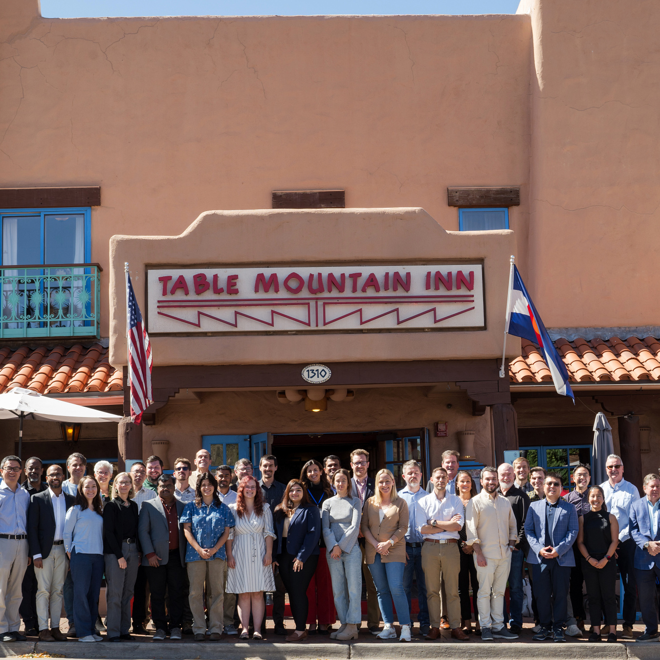 A group of 50 people stand outside in front of a building, smiling for the camera. 