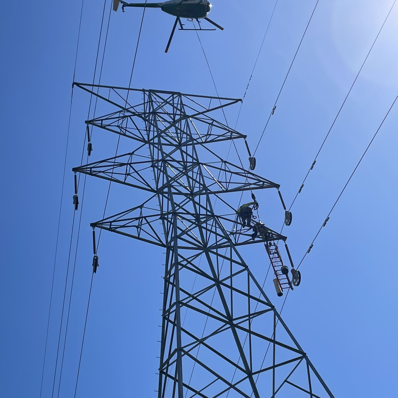 helicopter over transmission tower and lines. blue sky in background.