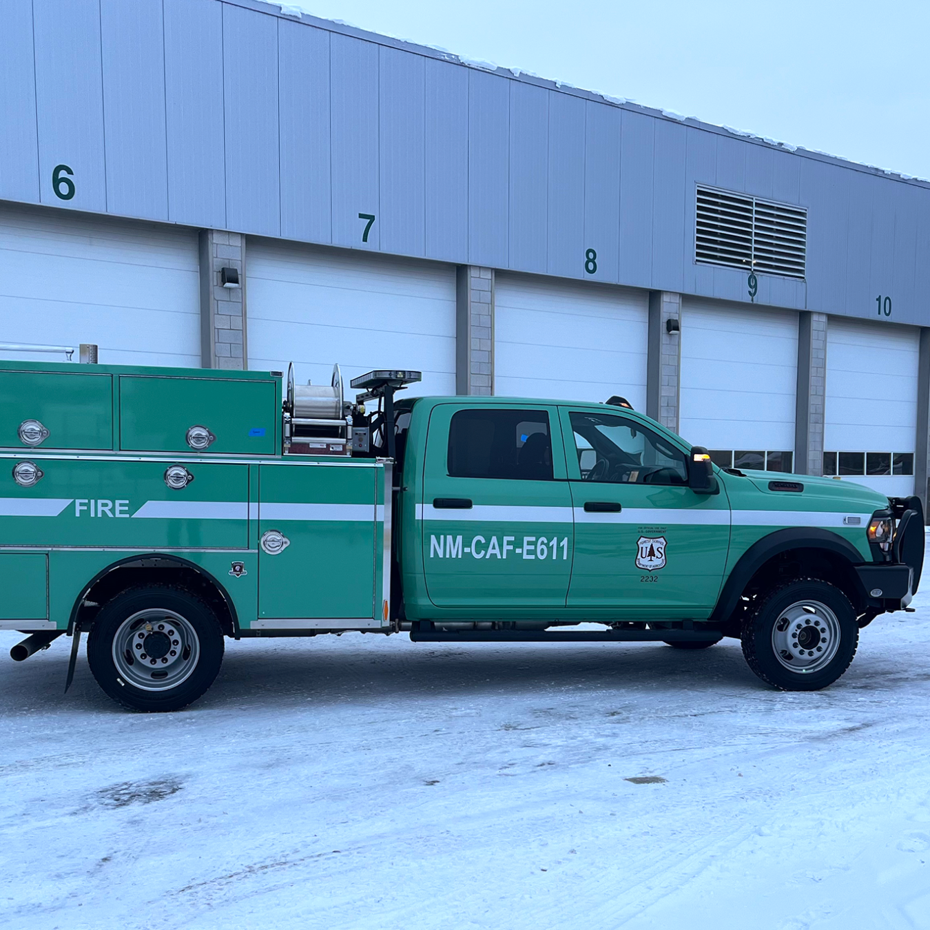 A green federal fleet truck in front of a garage building with multiple bays.