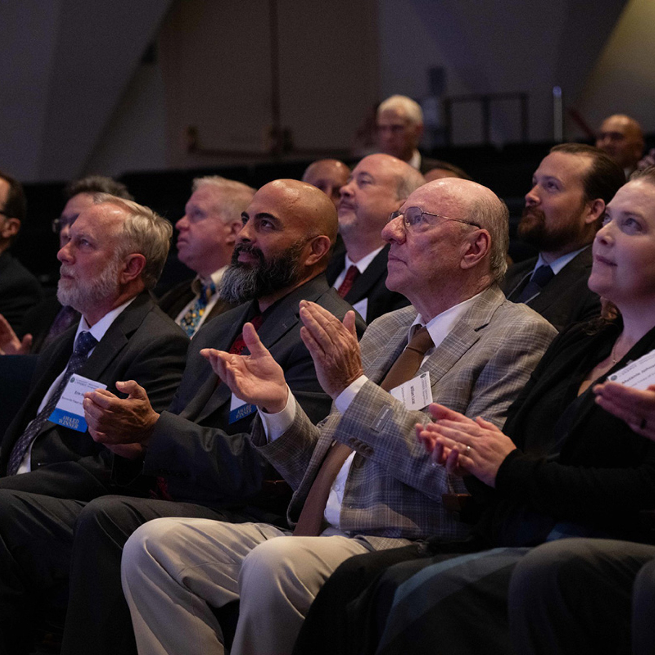 A seated audience clapping while looking at a stage (off screen).