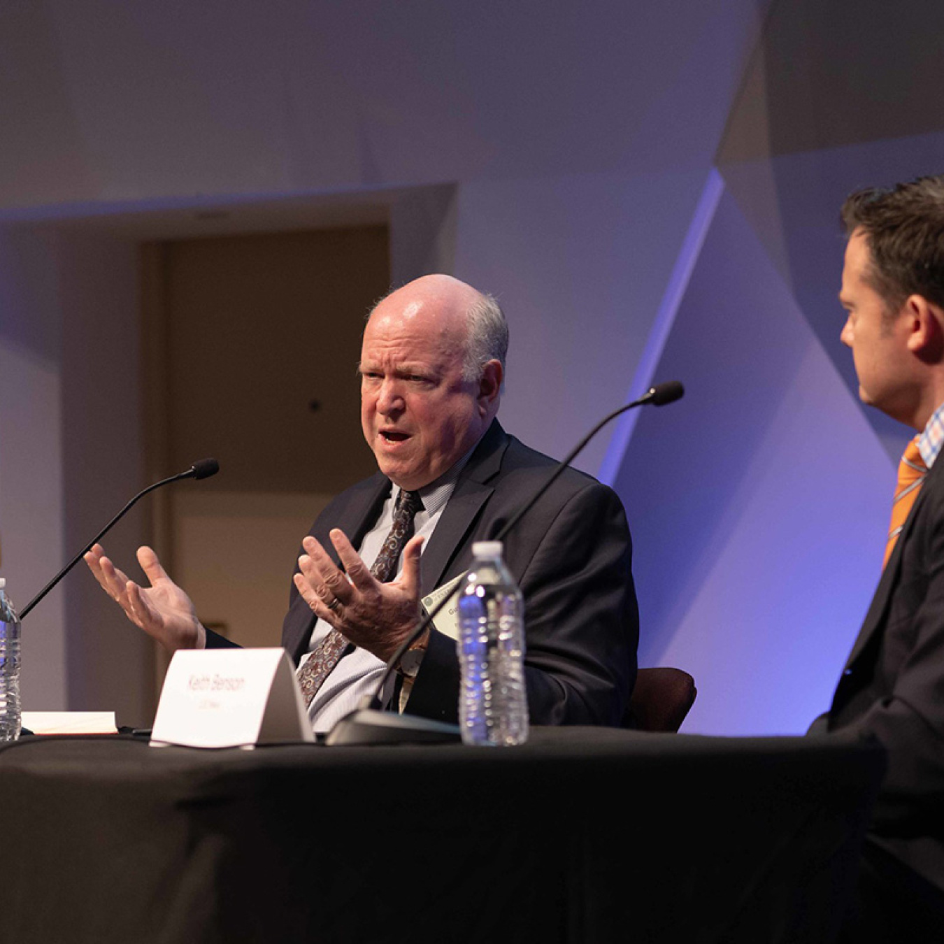Two individuals sitting at a table speaking into microphones.