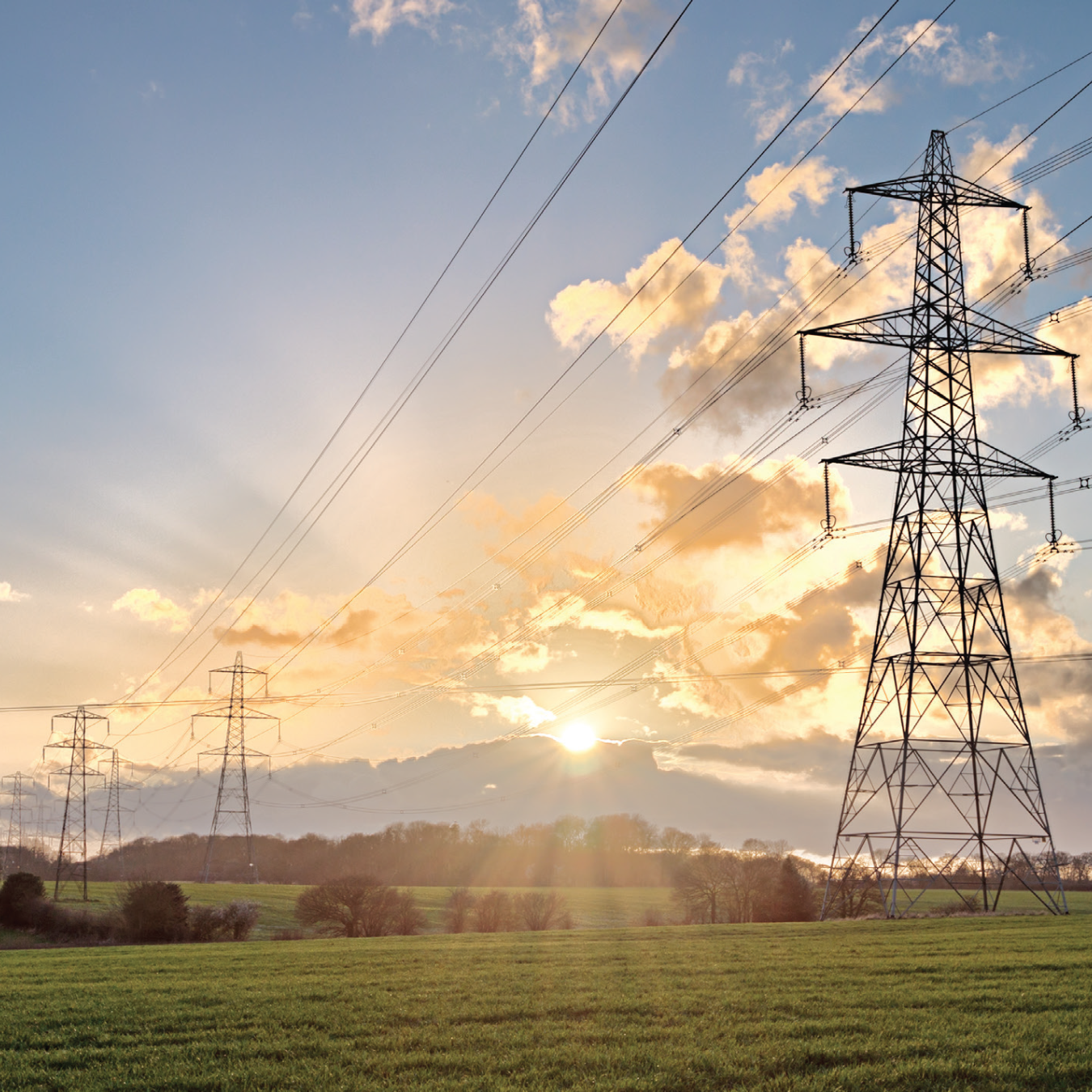 Transmission lines inside of a grassy area with cloudy skies.