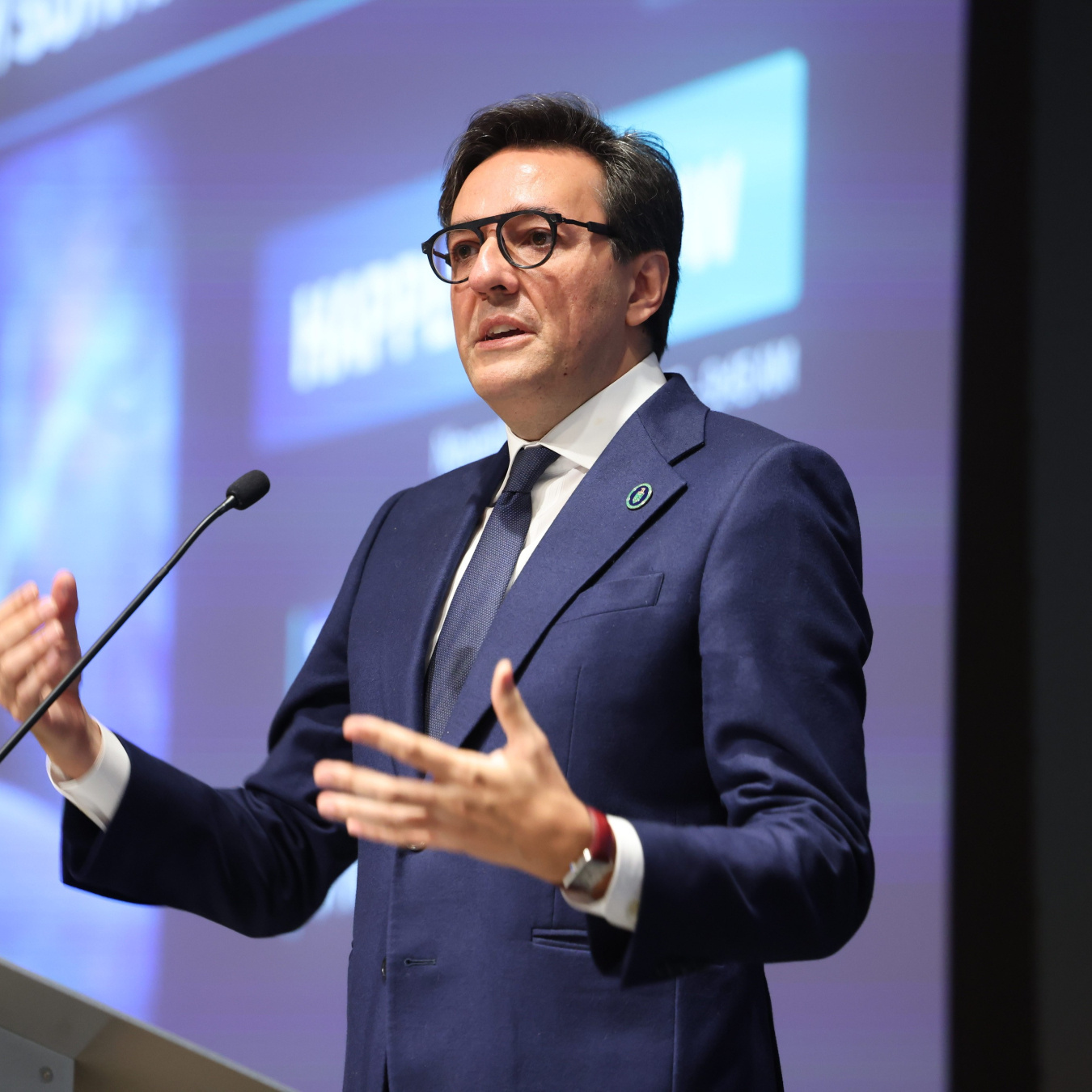 Darío Gil standing on a podium speaking with a large screen behind him. 