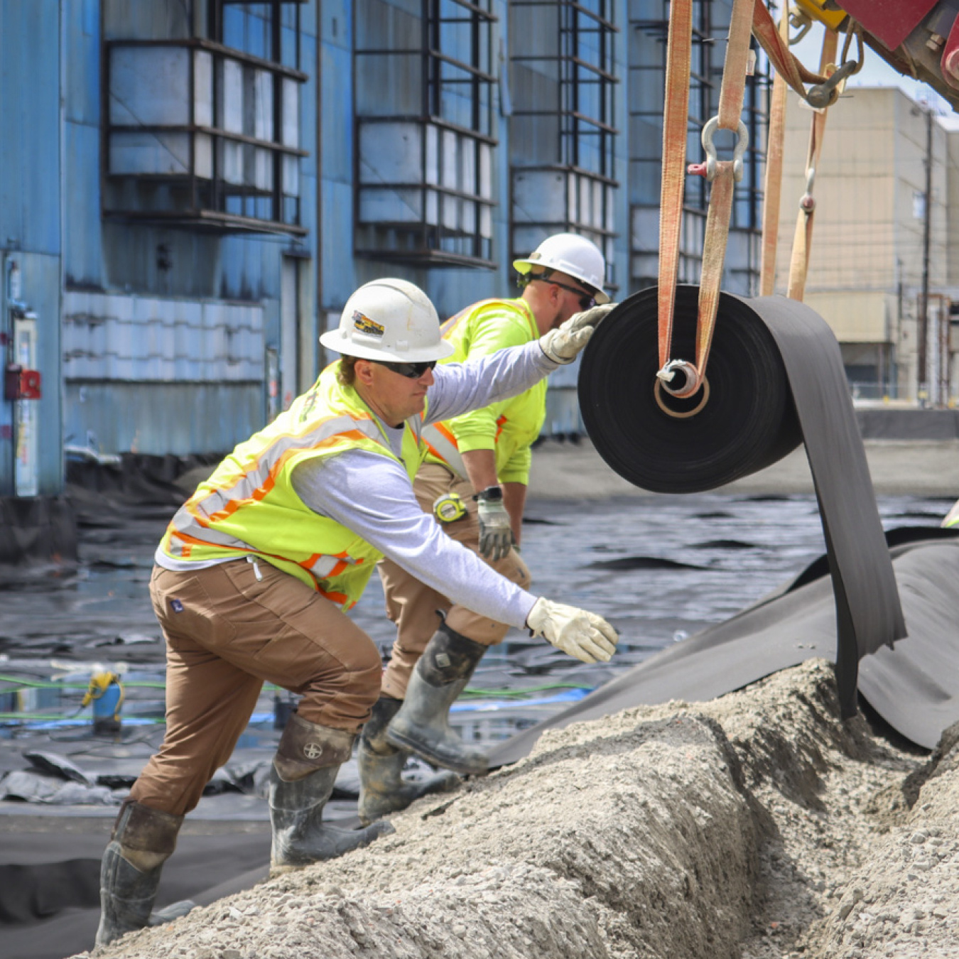 Workers in safety gear rolling out a large black cylinder
