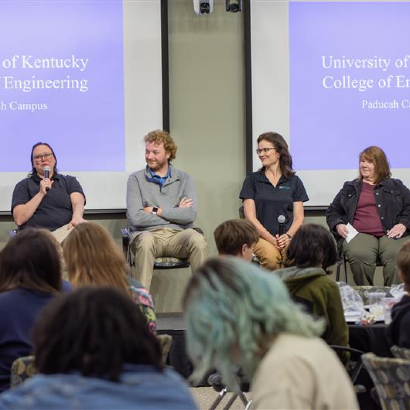 Four individuals sitting on stage participating in a panel in front of an audience