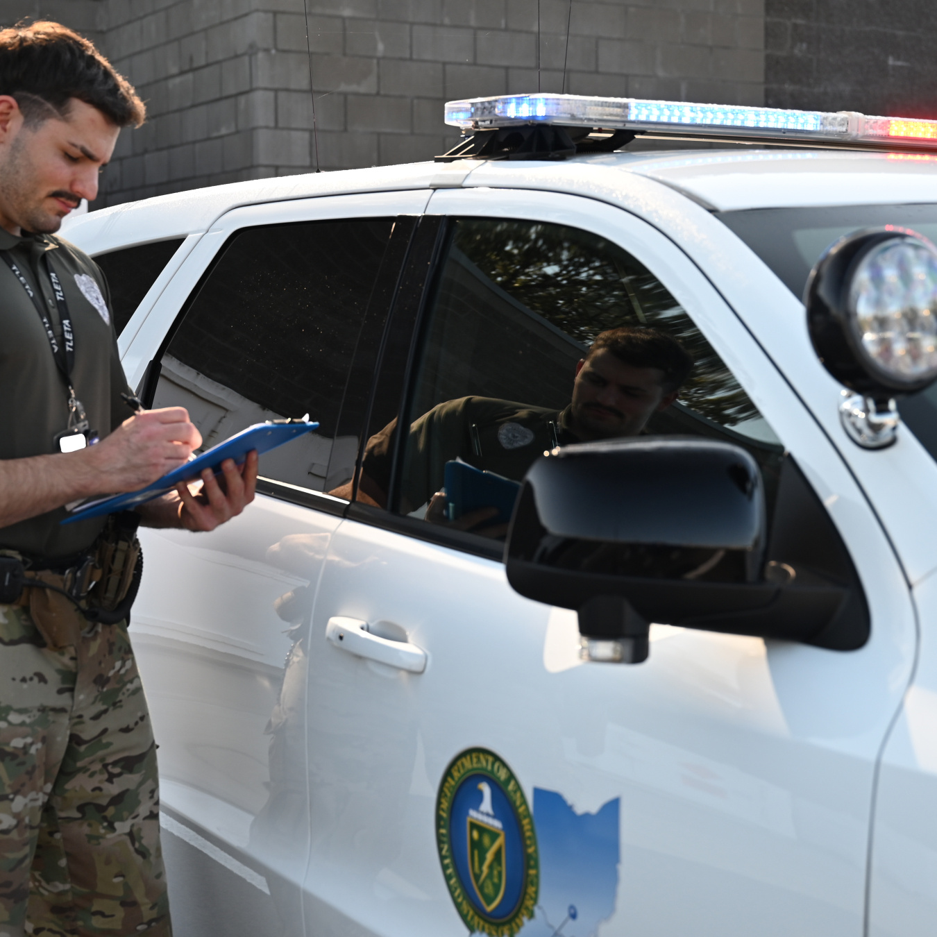 A protective officer at the Paducah site standing beside a white patrol car while holding and looking at a clipboard