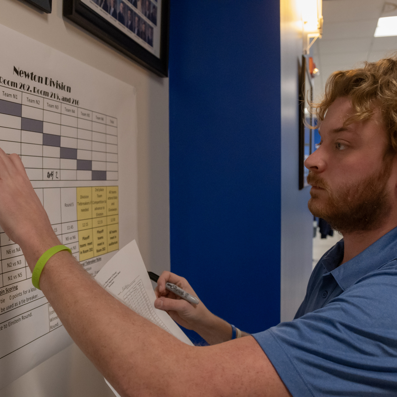 An employee in a blue shirt points at something written on a poster on the wall
