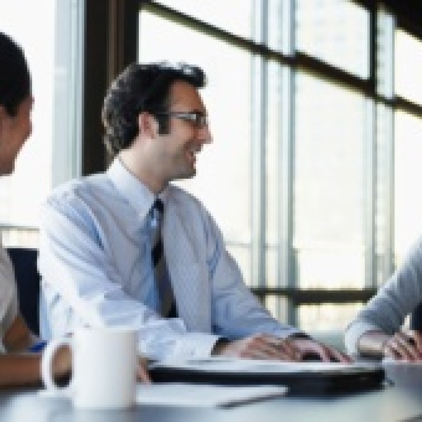 Three people in business attire sitting at a table talking / laughing.