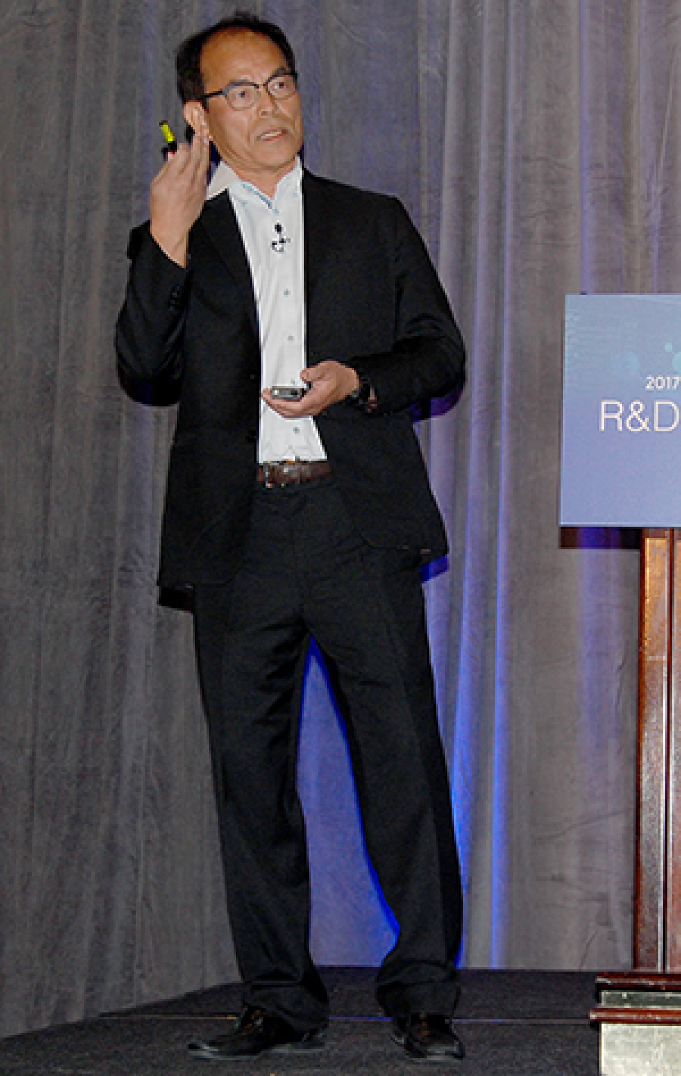 Man standing at the front of a convention hall, addressing the audience.