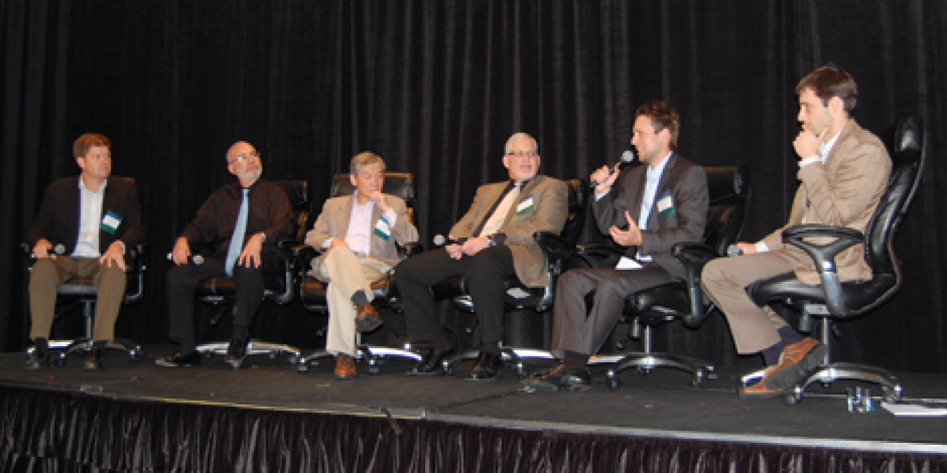 A row of six men seated on the stage, addressing the conference audience.