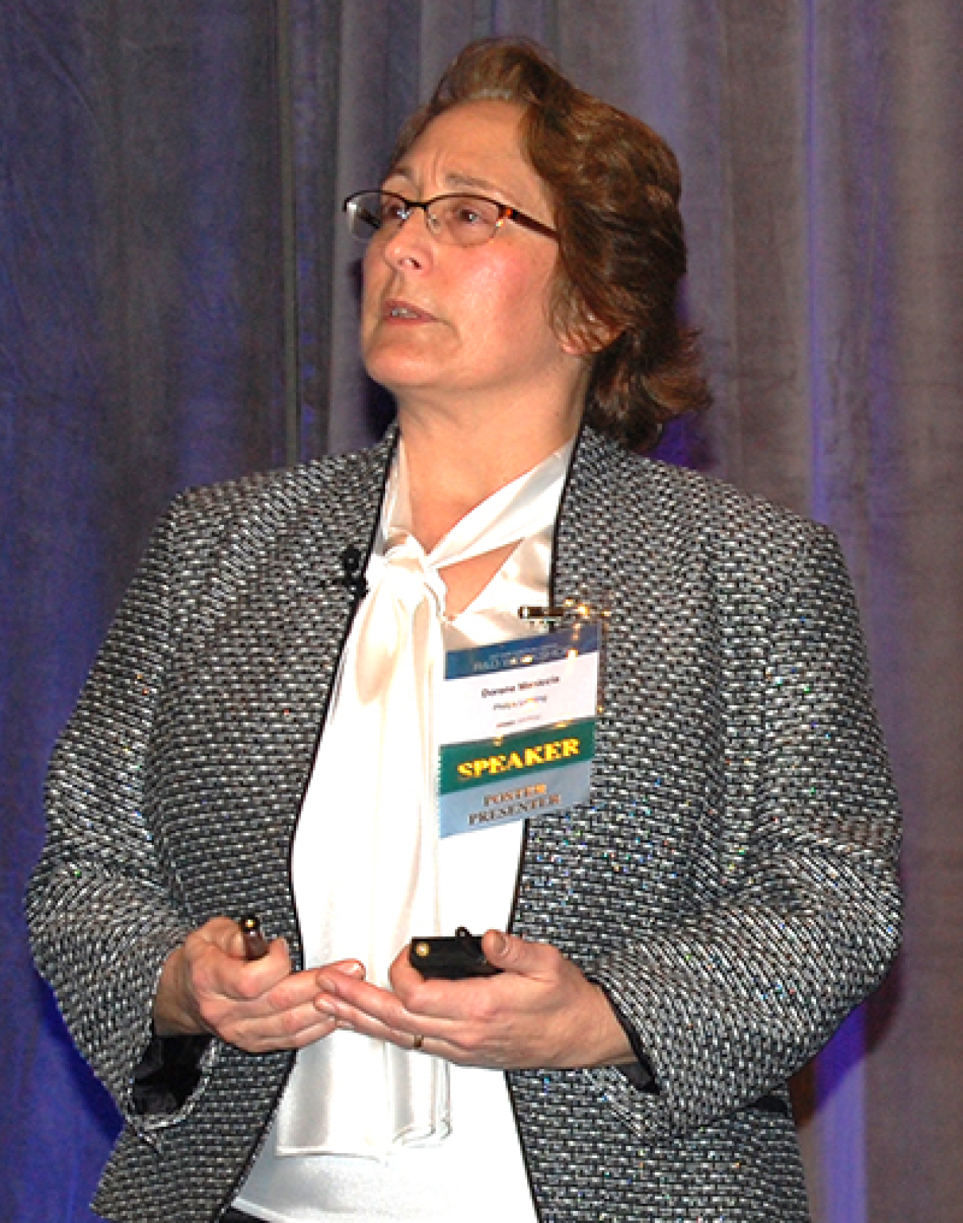 Woman standing at the front of a convention hall, addressing the audience.