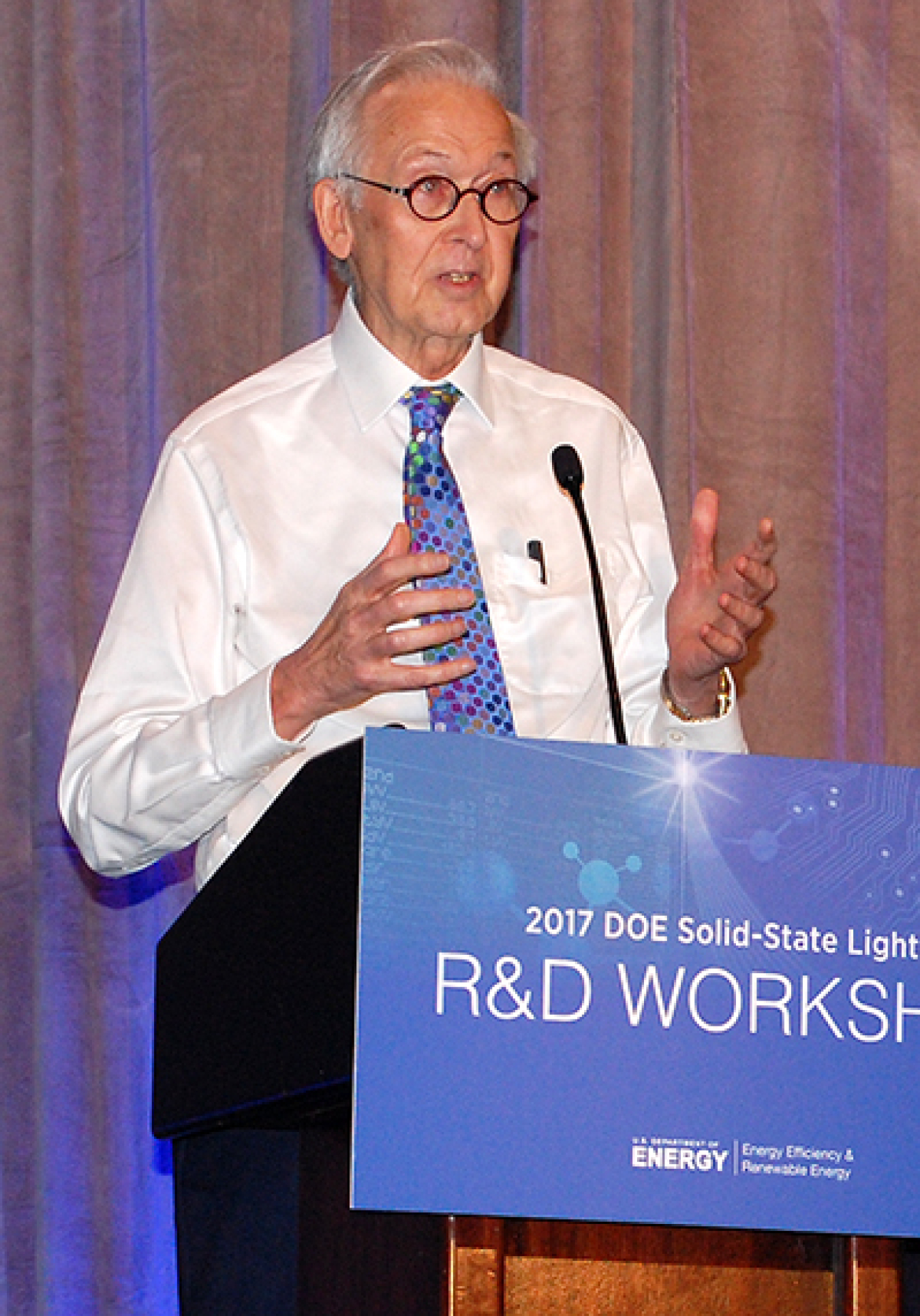 Man standing at the front of a convention hall, addressing the audience.