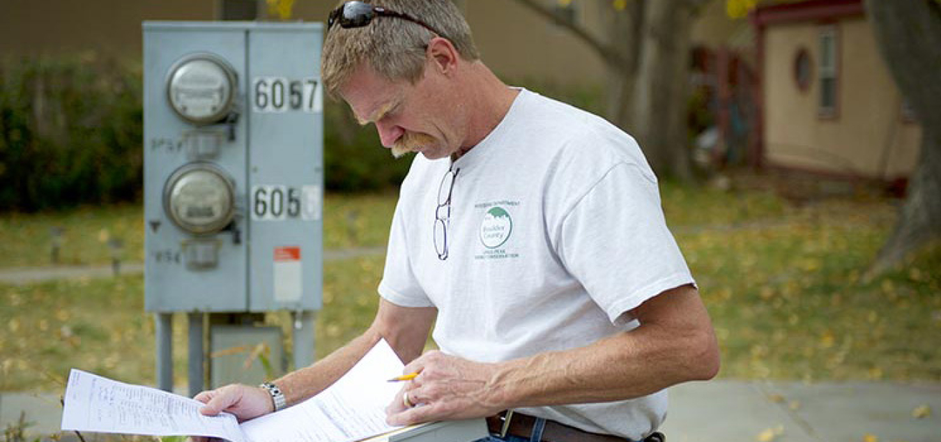 A worker reviews paperwork while standing next to a control box. 