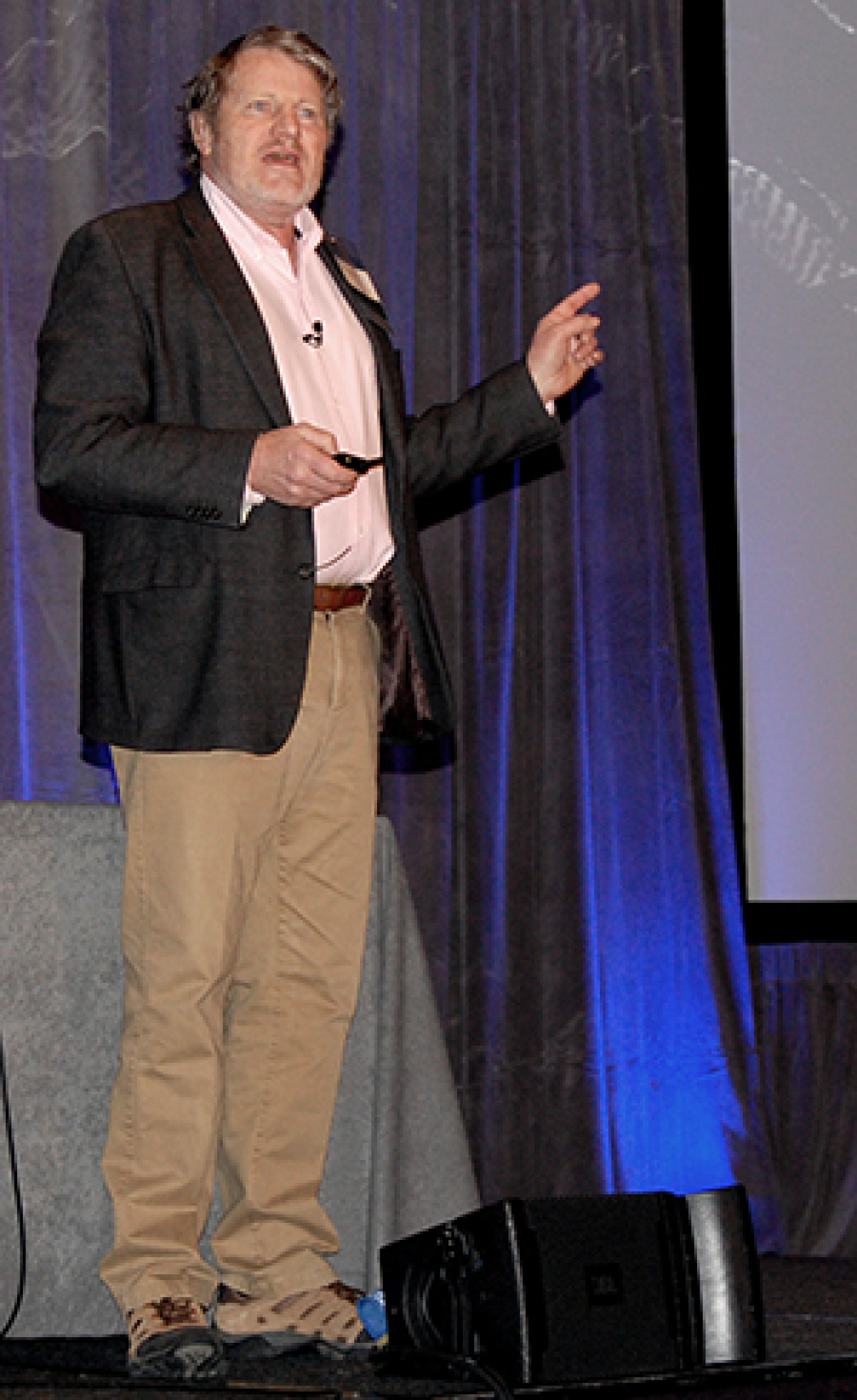 Man standing at the front of a convention hall, addressing the audience.