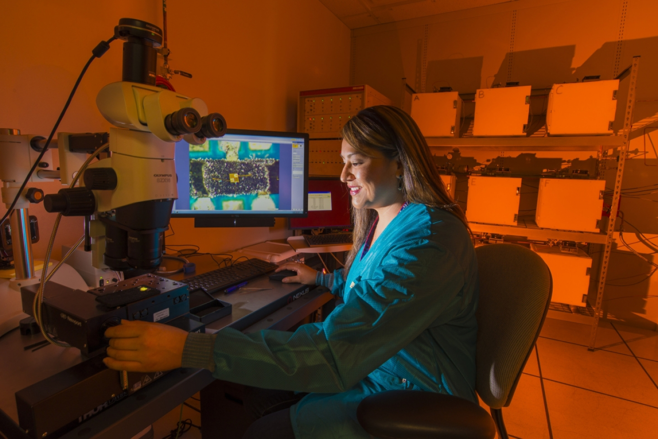 A woman sits by a computer monitor and is illuminated by its light. 