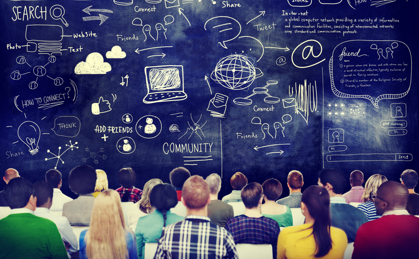 Photo of a group of people sitting in front of a giant chalkboard with lots of writing on it.