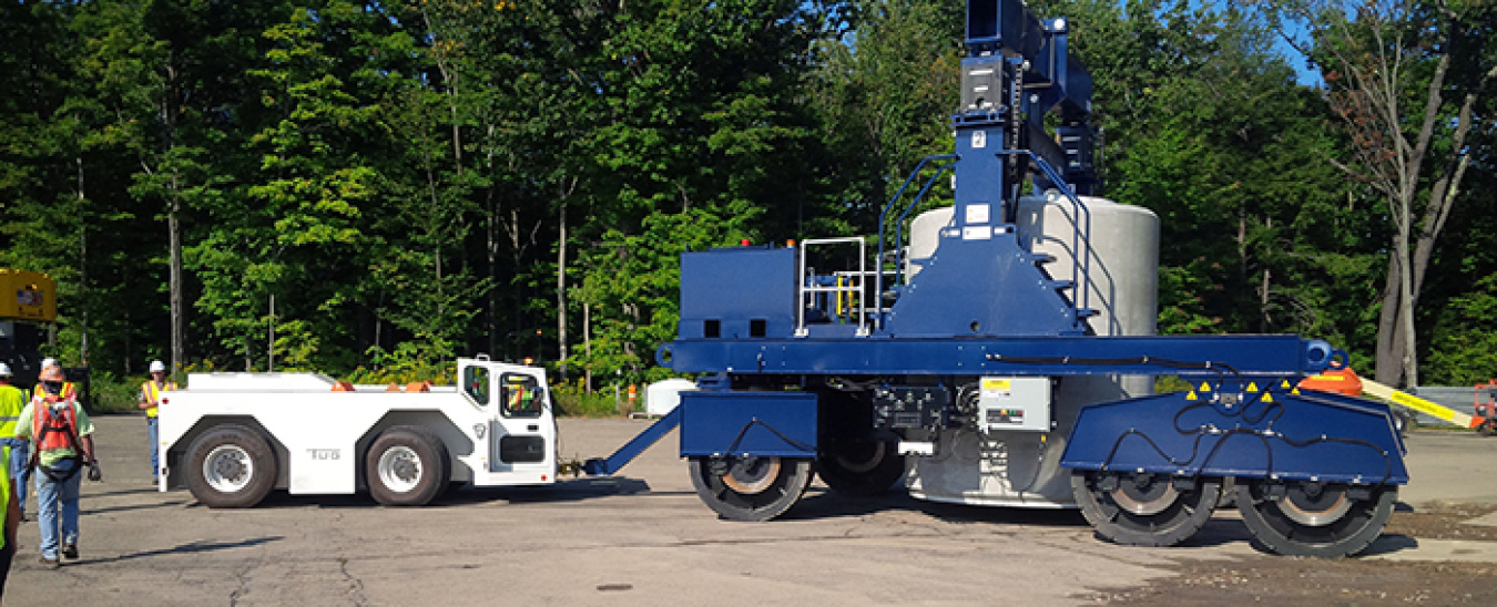A white “tug” pulls a blue vertical cask transporter.