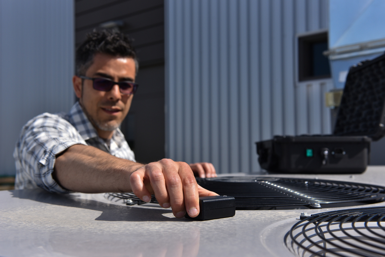 A man places a sensor on an HVAC system outside of an office building.