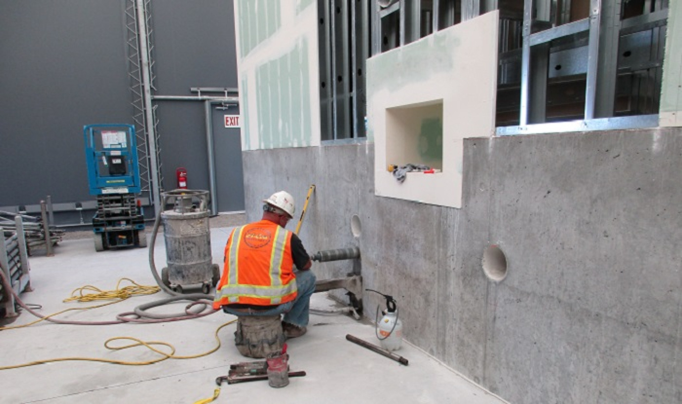 A worker drills a hole in the concrete wall of a mockup structure for the installation of remotely operated soil removal equipment.