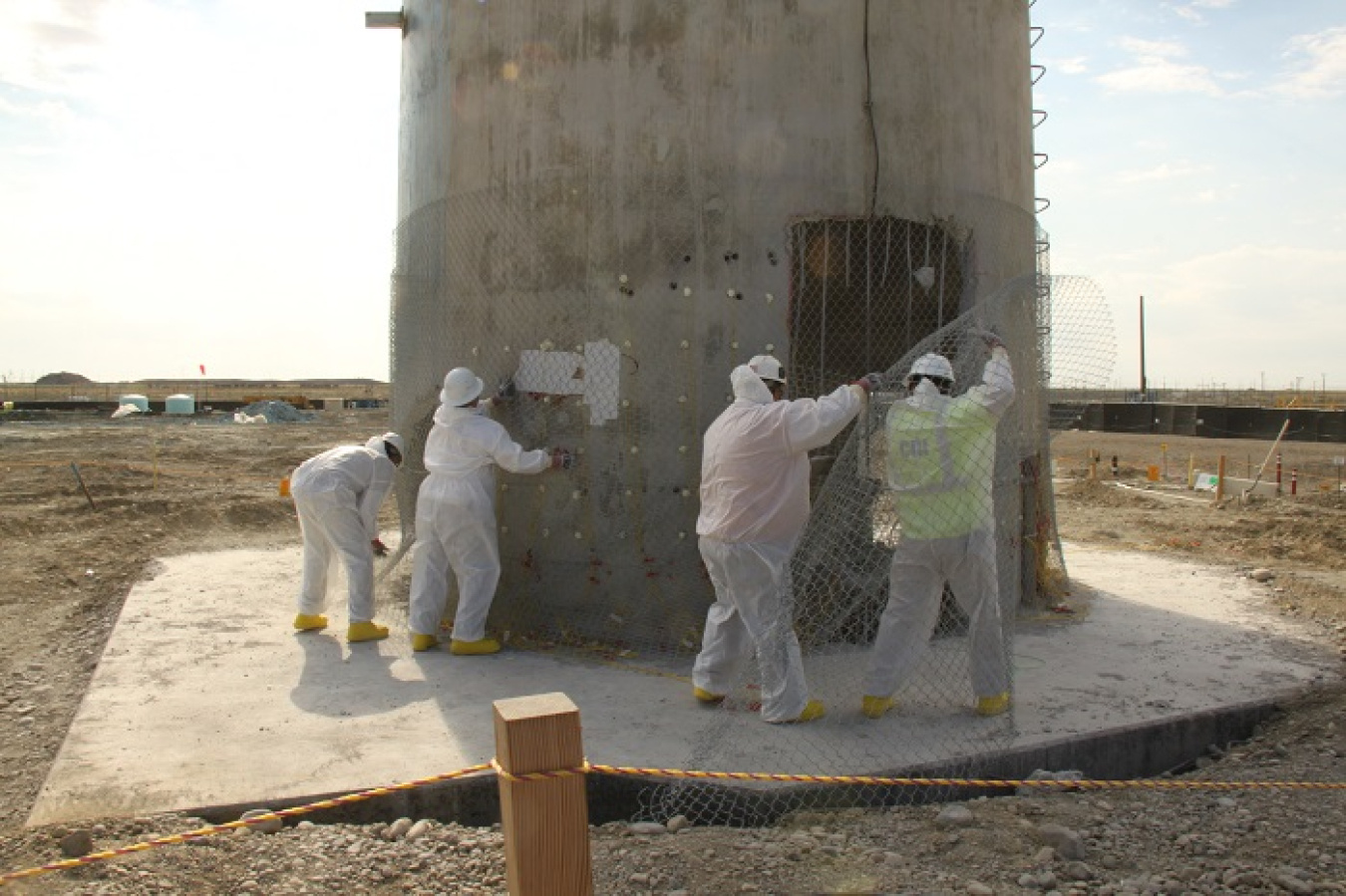 After placing explosives drilled in the base of the Plutonium Finishing Plant’s ventilation stack, workers wrapped chain-link fence around the stack to limit the spread of debris from the explosion.